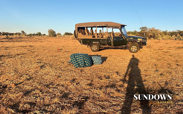 Sundowner drinks set beside a safari Land Cruiser at golden hour, Sundown Safaris Sundowner package